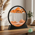 Orange moving sand art picture in a round black frame with display stand on a wooden table